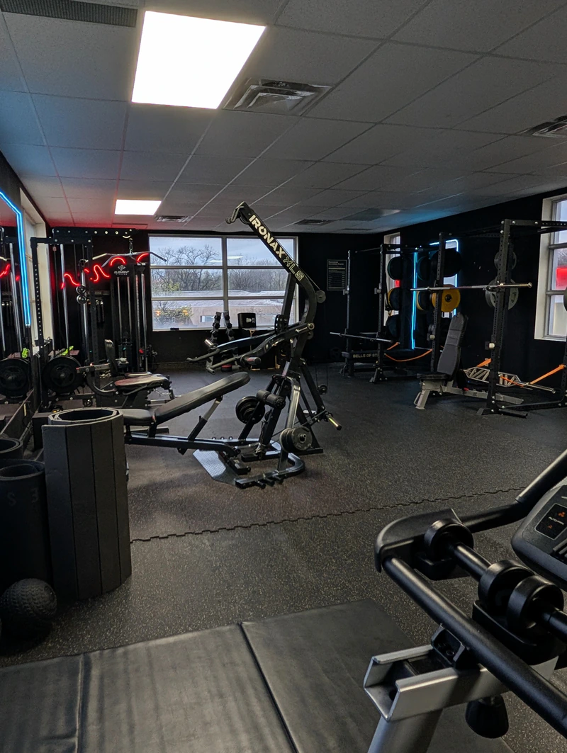 Strength floor at Retraine in Pickering with plate-loaded machines and squat racks lit by blue and red neon.